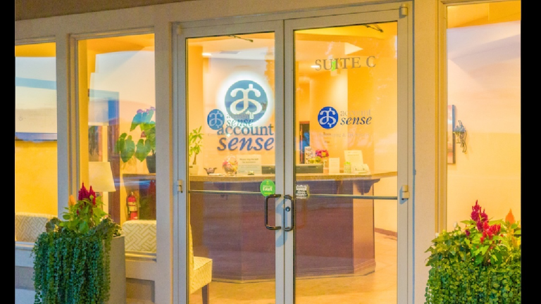 Front entrance of an office with glass doors displaying the logo ‘Account Sense’ and a view of the reception area inside.