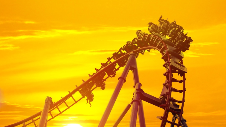 Roller coaster ascending a steep loop at sunset, framed by a vivid orange sky.